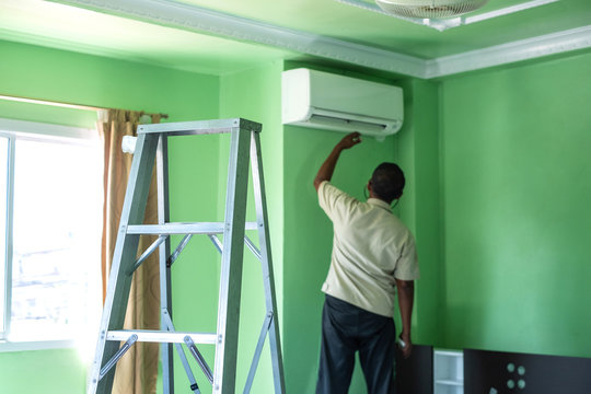 Workers repairs and cleans the air conditioner in the room. Steel ladder used by the worker to climb up to close to the air conditioner.
