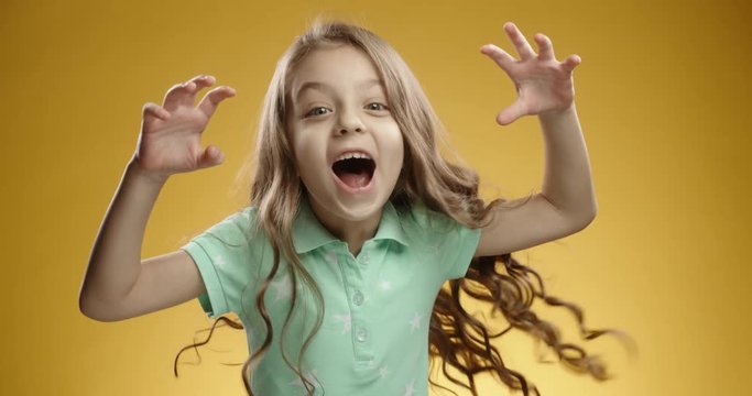 Cute caucasian girl scaring someone, looking at camera than bursting into laugther. Cheerful child expressing positive emotions, isolated on yellow background close up 4k