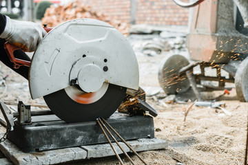 Construction worker cutting steel bar using electric grinder cutting metal.