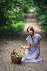 Gorgeous girl with piggy tails in blue floral dress sitting in the middle of the road with her basket full with flowers