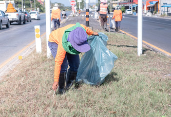 Group of environmental activists picking up trash on hightway road during very hot day.