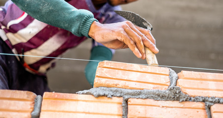 Close up of bricklayer worker's hand installing red brick with trowel putty knife for new house building at construction site.