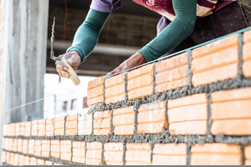 Close up of bricklayer worker's hand installing red brick with trowel putty knife for new house building at construction site.