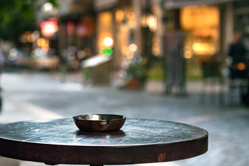 Obraz premium A bar round wooden table with an ashtray, outdoors in the evening, copy space.