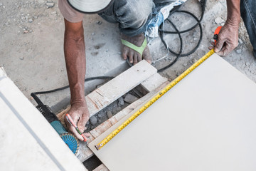 Top view of worker measuring ceramic tile using measure tape and marker prepare for installing at construction site for new house building