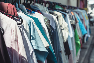 Selective focus and close up of many colorful of second hand clothes hanging on hanger in a row.