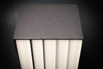 A set of five monochromatic cloth-bound books stored inside a black hard cardboard slipcase set on a slightly graduated and subtly textured dark background.
