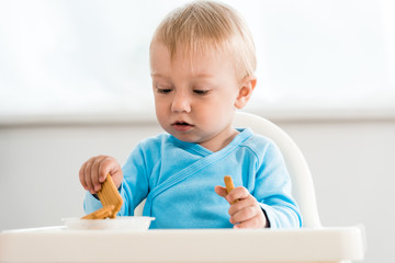 cute toddler kid sitting in feeding chair near tasty cookies at home