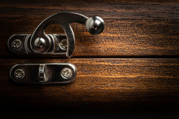An elegant metal sliding clasp lock screwed into the lid of a wooden box.