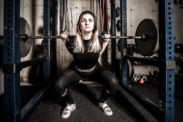 Fototapeta na wymiar Young woman weight training in a gritty basement gym.