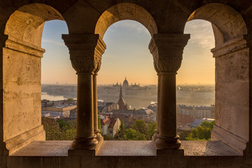 Fototapeta na wymiar Aerial view of the Parliament of Hungary through Gothic windows of Fisherman's Bastion (Halaszbastya) at sunrise with beautiful sky and clouds , Budapest, Hungary