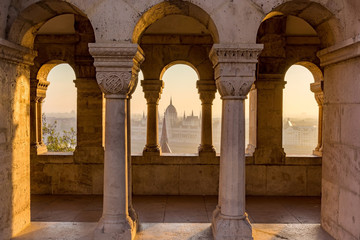 Aerial view of the Parliament of Hungary through Gothic windows of Fisherman's Bastion (Halaszbastya) at sunrise with beautiful sky and clouds , Budapest, Hungary