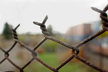 The upper links of a rustyold chain link fence with railroad cars in the background.