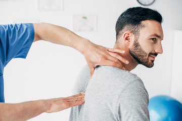 chiropractor massaging neck of good-looking man in hospital - obrazy, fototapety, plakaty