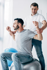 chiropractor stretching arms of patient on fitness ball in hospital