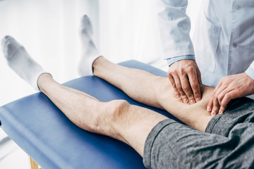 partial view of Physiotherapist massaging leg of man on massage table in hospital