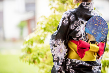 浴衣を着た30代のきれいな女性が緑の前に立って彼を待っている