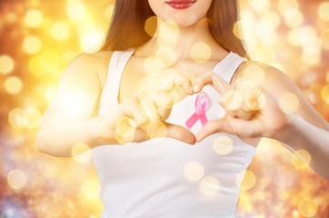 Heart framing from fingers on woman chest with pink badge to support breast cancer cause, PS: you can change the ribbon color to red to support AIDS cause as both using same symbol