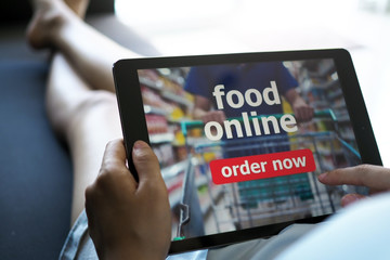 Women use tablets to order food online while lying on the couch at home.