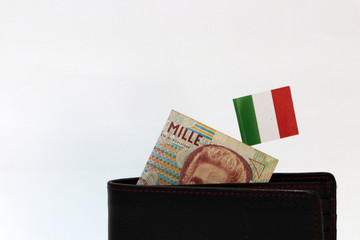 One thousand Lire of Italy banknote and mini Italia nation flag stick on the black wallet with white background.