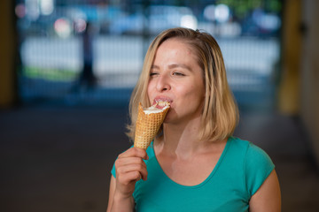 Portrait of a cute girl in a green dress is walking outside and eating dessert. Beautiful blonde enjoying a cone with ice cream on a beautiful summer day. Life is a pleasure