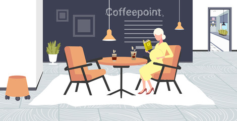 pregnant woman reading book sitting at cafe table girl touching her belly pregnancy and motherhood concept modern coffee point interior flat full length horizontal
