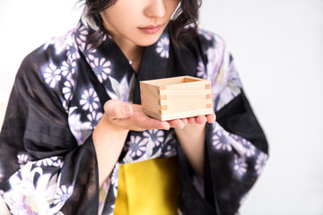 浴衣を着た30代のきれいな女性が白背景で升で日本酒をのんでいる