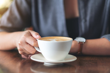 Closeup image of a woman holding and drinking hot coffee in cafe