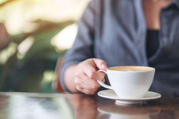 Closeup image of a woman holding and drinking hot coffee in cafe