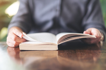 Closeup image of a woman holding and reading a vintage novel book on wooden table