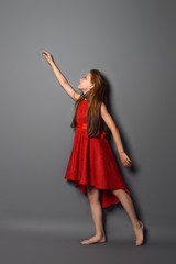 growth Studio portrait of a red-haired teenage girl in a red dress.  gray background. The girl is standing against a wall and raised his hand as if in flight