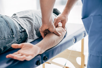 partial view of chiropractor massaging arm of patient in hospital