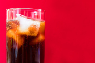 A glass of cola with ice on a red background. Concept for non-alcoholic cool drinks. Close-up..Copy space