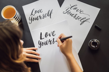 Love yourself. Calligrapher Young Woman writes phrase on white paper. Inscribing ornamental...