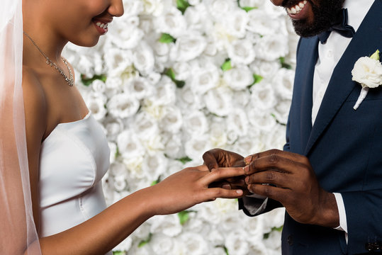 Cropped View Of Cheerful African American Man Putting Wedding Ring On Finger Of Bride Near Flowers