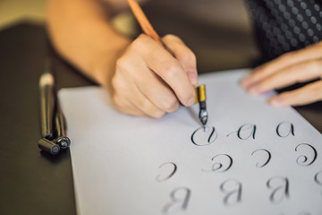 Calligrapher Young Woman writes phrase on white paper. Inscribing ornamental decorated letters....