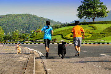 Couple woman running together with brown and black dogs in the park.