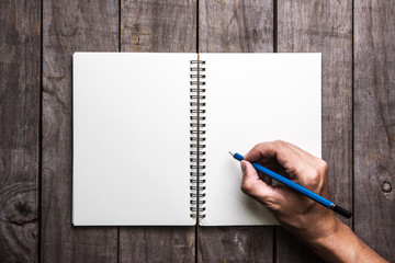 male hand is writing in a big notepad on a wooden table