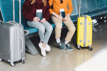cropped view of preteen kids sitting in waiting hall with passports and suitcases