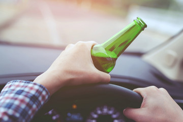 close up hand Drunk young man while driving a car with a bottle of beer. Don't drink and drive concept. Driving while intoxicated the danger may be a death.