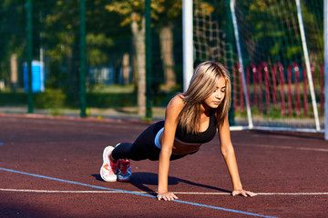 Sport girl. The girl is doing fitness exercises. Beautiful young sports woman doing exercises. A woman is training on a sports field. Young beautiful girl in sports uniform posing on sports field.
