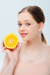 smiling beautiful teenage girl holding ripe orange half isolated on grey
