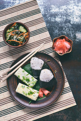 Mix of Japanese food - rice balls onigiri, omelette, pickled ginger, sunomono wakame cucumber salad and chopsticks. Asian breakfast or lunch background