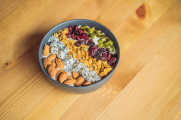 Mango smoothies bowl with almond, dragon fruit, dried cherries, pumpkin seeds and granola on wooden background