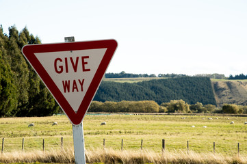 Give Way is warning sign on the roadside in New Zealand with green meadow and tree background.