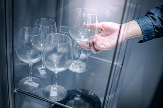 Male hand picking empty wine glass from tempered glass cabinet in the kitchen. Drinking glassware concept