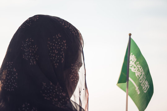 Muslim Woman In Scarf With Saudi Arabia Flag Of At Sunset.Concept