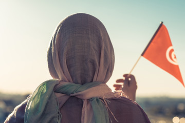 Muslim woman in scarf with Tunisia flag of at sunset.Concept