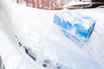 blue sponge and soap over the car for washing. Motor hood front being cleaned. Concept car wash clean.