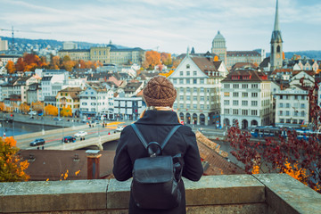 Young blonde tourist girl in warm hat and coat with backpack walking at cold autumn in Europe city enjoying her travel in Zurich Switzerland - obrazy, fototapety, plakaty